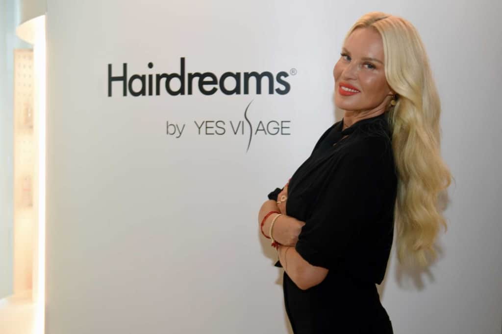 Woman with long blond hair poses in front of the Flagship Store Logo