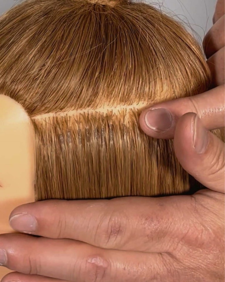 A hairdresser shows the mini micro bondings on a training head on a